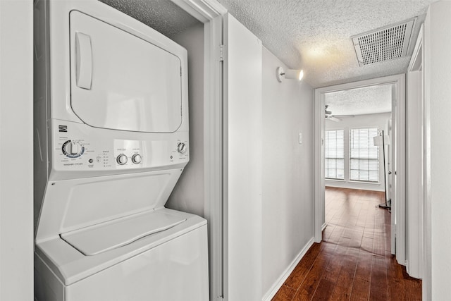 clothes washing area with ceiling fan, dark wood-type flooring, stacked washing maching and dryer, and a textured ceiling