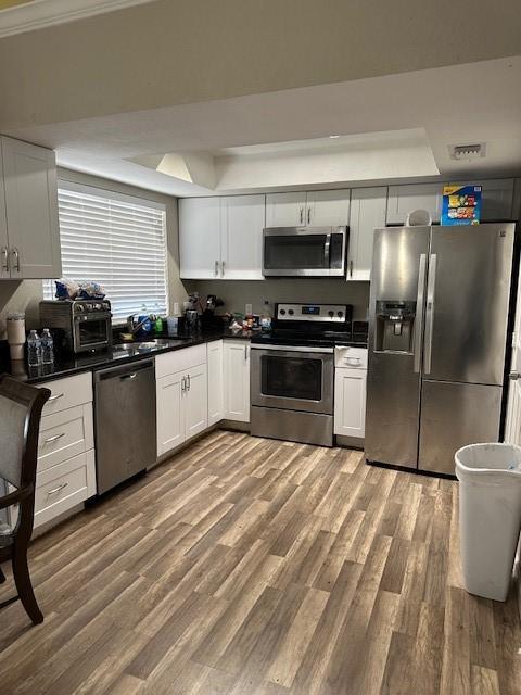 kitchen with a tray ceiling, white cabinetry, stainless steel appliances, and wood-type flooring