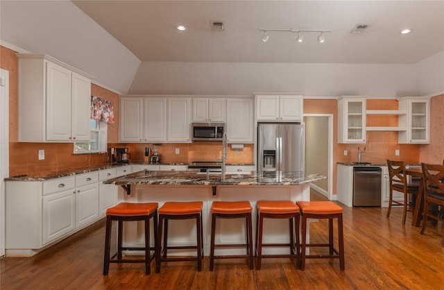 kitchen featuring a center island with sink, white cabinets, dark stone counters, and appliances with stainless steel finishes