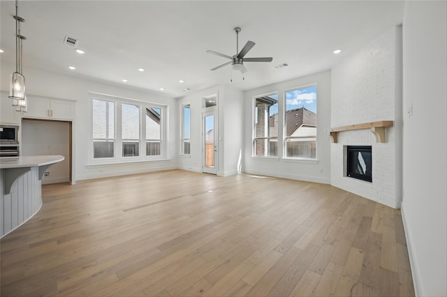 unfurnished living room featuring a brick fireplace, light wood-style flooring, a ceiling fan, baseboards, and visible vents