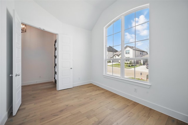 spare room featuring light wood-style floors, baseboards, and lofted ceiling