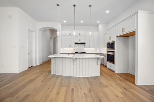 kitchen featuring oven, arched walkways, white cabinetry, and built in microwave