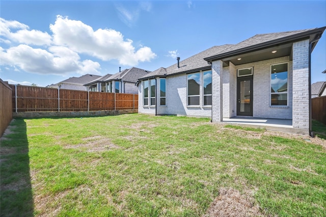 rear view of house featuring a fenced backyard, a yard, a patio area, and brick siding