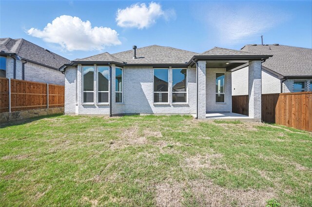 back of house with roof with shingles, a lawn, brick siding, a fenced backyard, and a patio