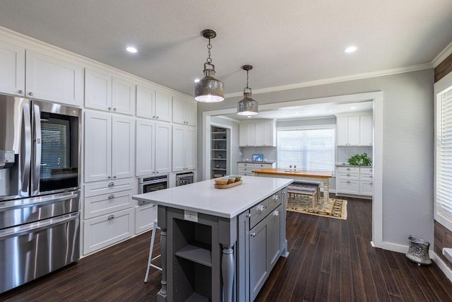 kitchen with decorative backsplash, stainless steel appliances, pendant lighting, white cabinets, and a center island