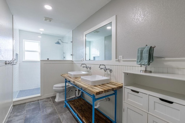 bathroom with toilet, dual sinks, and a tile shower