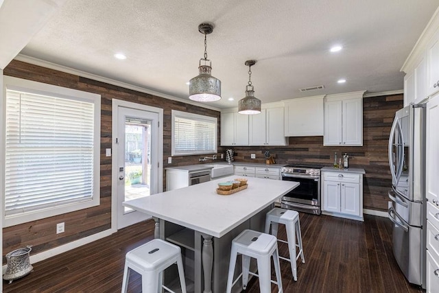 kitchen featuring pendant lighting, a center island, appliances with stainless steel finishes, a kitchen bar, and white cabinetry