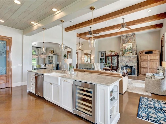 kitchen featuring a sink, wine cooler, arched walkways, a stone fireplace, and white cabinets