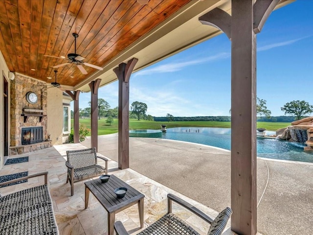 view of patio with an outdoor pool, an outdoor stone fireplace, a ceiling fan, and a water view