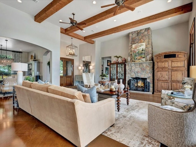 living room featuring beamed ceiling, ceiling fan with notable chandelier, arched walkways, a high ceiling, and a fireplace