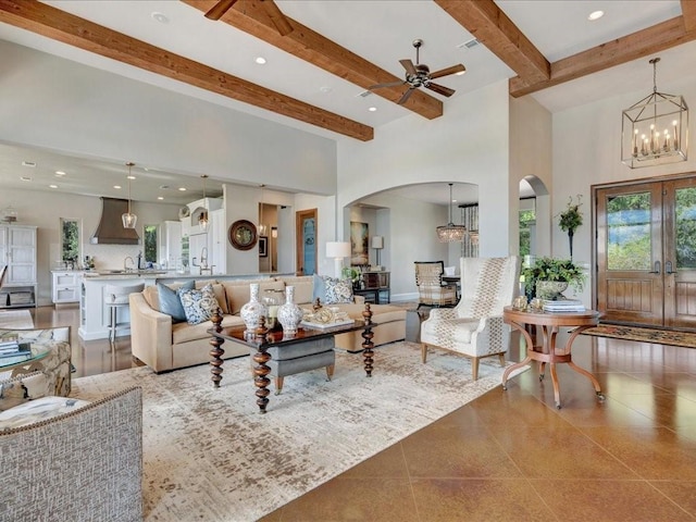 living area featuring beamed ceiling, recessed lighting, ceiling fan with notable chandelier, a towering ceiling, and arched walkways