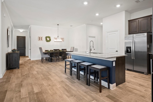 kitchen featuring light stone countertops, sink, stainless steel fridge with ice dispenser, a kitchen island with sink, and dark brown cabinets