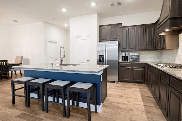 kitchen with light stone countertops, appliances with stainless steel finishes, sink, light hardwood / wood-style flooring, and an island with sink