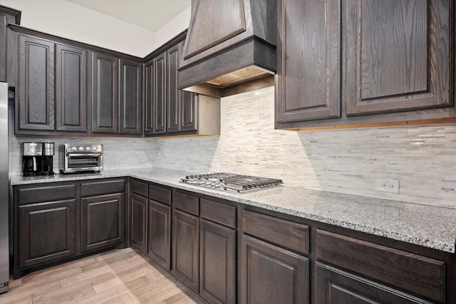 kitchen featuring light stone countertops, tasteful backsplash, dark brown cabinets, light hardwood / wood-style floors, and stainless steel gas cooktop