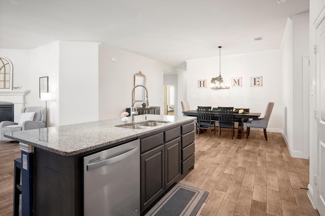 kitchen with a center island with sink, sink, stainless steel dishwasher, light stone countertops, and light hardwood / wood-style floors