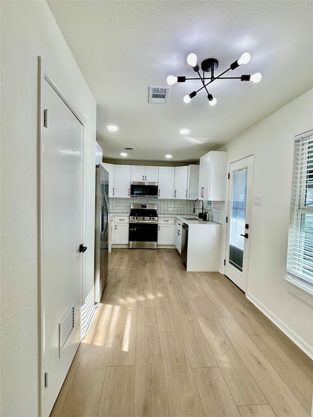 kitchen with backsplash, white cabinets, sink, appliances with stainless steel finishes, and a chandelier