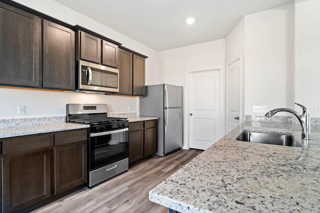 kitchen with dark brown cabinetry, light stone countertops, sink, and stainless steel appliances