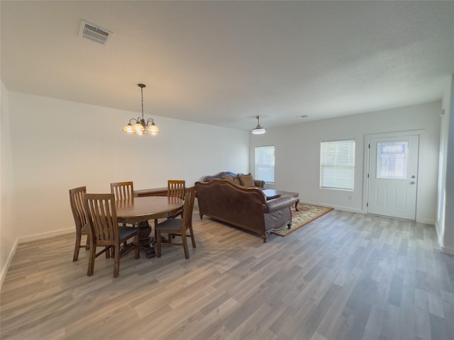 dining area with wood-type flooring, a healthy amount of sunlight, and a chandelier