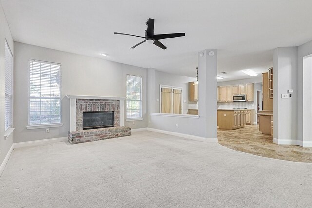 unfurnished living room with ceiling fan, light colored carpet, and a brick fireplace