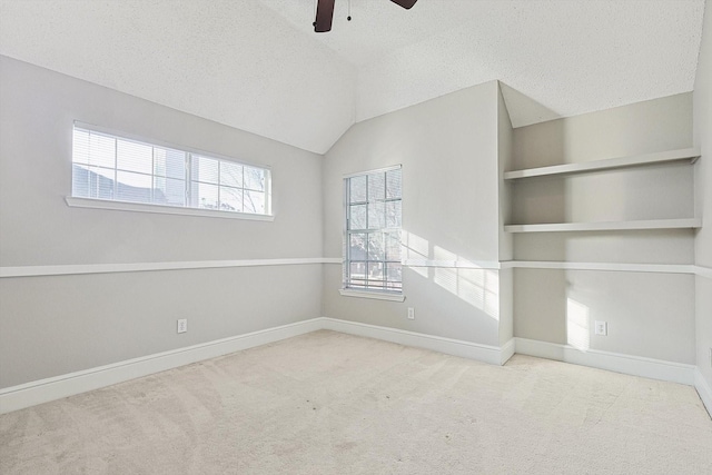 empty room featuring built in shelves, ceiling fan, light colored carpet, lofted ceiling, and a textured ceiling