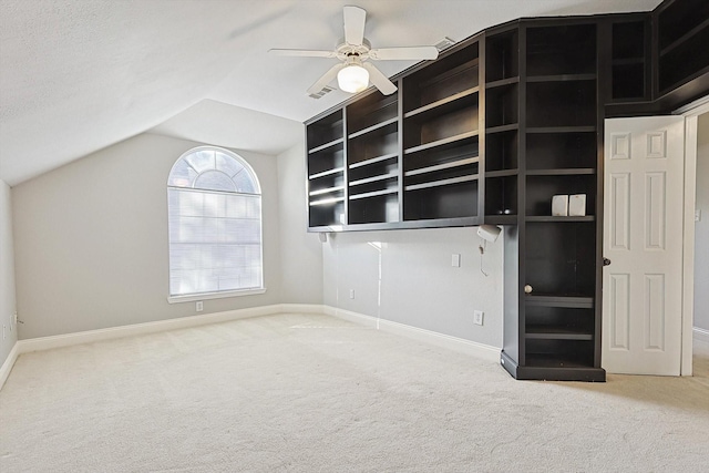 empty room featuring built in features, carpet floors, vaulted ceiling, and ceiling fan