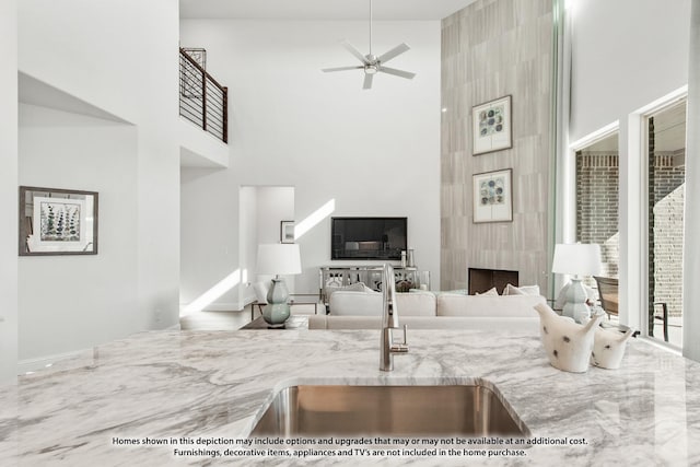 living room featuring ceiling fan, a fireplace, a towering ceiling, and sink