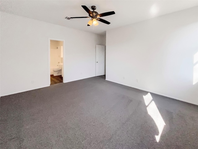 unfurnished bedroom featuring ceiling fan, dark carpet, and connected bathroom