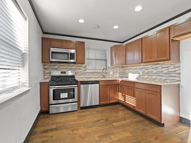 kitchen with dark wood-type flooring, appliances with stainless steel finishes, tasteful backsplash, light stone counters, and ornamental molding