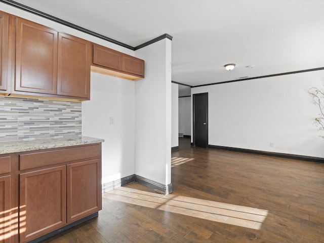 kitchen with light stone counters, dark wood-type flooring, tasteful backsplash, and ornamental molding