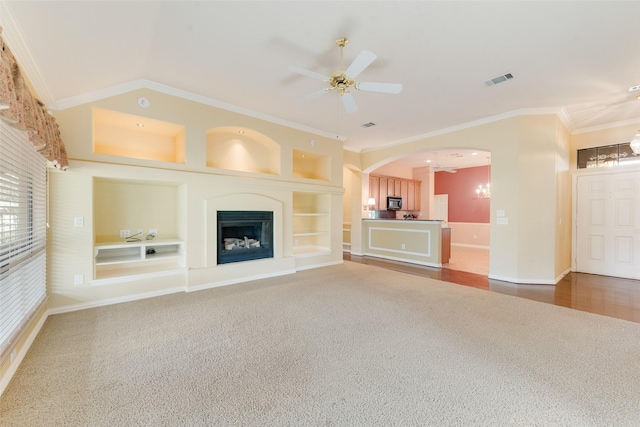 unfurnished living room featuring built in shelves, ornamental molding, ceiling fan with notable chandelier, and carpet floors