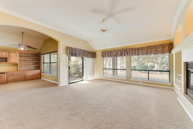 unfurnished living room with ornamental molding, built in shelves, light colored carpet, vaulted ceiling, and ceiling fan