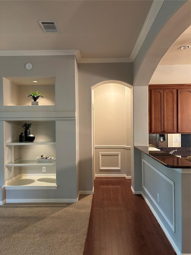 10104 Southpoint Ct, Denton, TX 76207 - kitchen featuring crown molding, arched walkways, dark countertops, built in shelves, and dark wood-style flooring