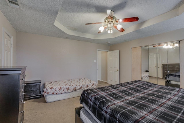 carpeted bedroom with ceiling fan, a raised ceiling, a textured ceiling, and a closet