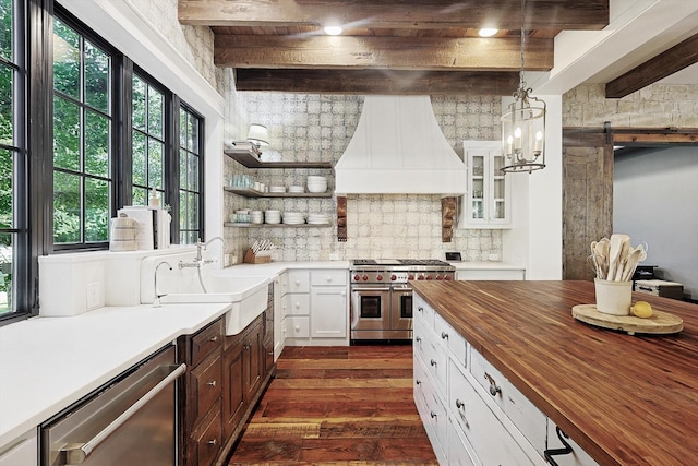 kitchen featuring butcher block counters, sink, custom range hood, beamed ceiling, and stainless steel appliances