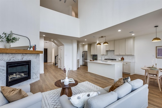 living room with recessed lighting, a high end fireplace, baseboards, stairs, and light wood-style floors