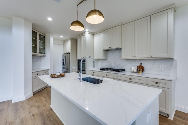 kitchen with glass insert cabinets, light stone counters, hanging light fixtures, stainless steel appliances, and a sink