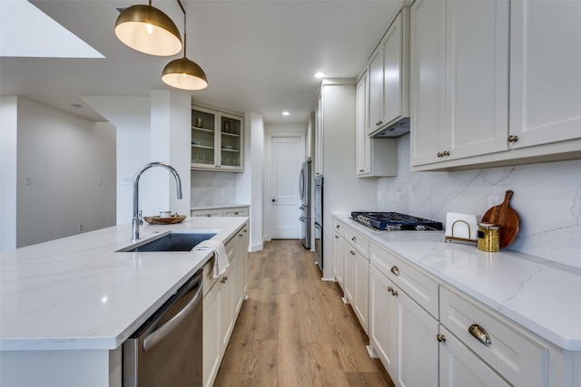 kitchen with glass insert cabinets, hanging light fixtures, stainless steel appliances, white cabinetry, and a sink