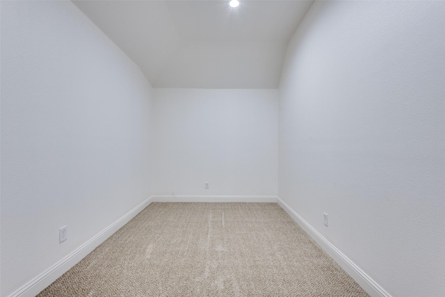 carpeted spare room featuring vaulted ceiling and baseboards