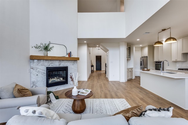 living area with recessed lighting, a high ceiling, a fireplace, baseboards, and light wood finished floors