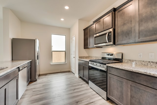 kitchen with dark brown cabinetry, light stone counters, light wood-type flooring, and appliances with stainless steel finishes