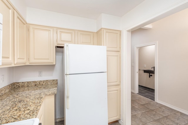 kitchen with cream cabinets, white refrigerator, and light stone counters