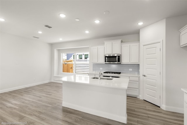 kitchen with white cabinetry, sink, tasteful backsplash, light hardwood / wood-style flooring, and an island with sink