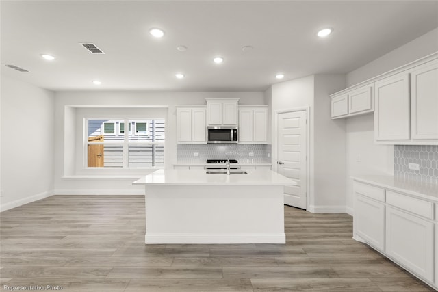 kitchen with a center island with sink, backsplash, white cabinetry, and sink