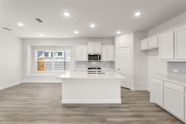 kitchen featuring light countertops, backsplash, a sink, stainless steel microwave, and white cabinetry