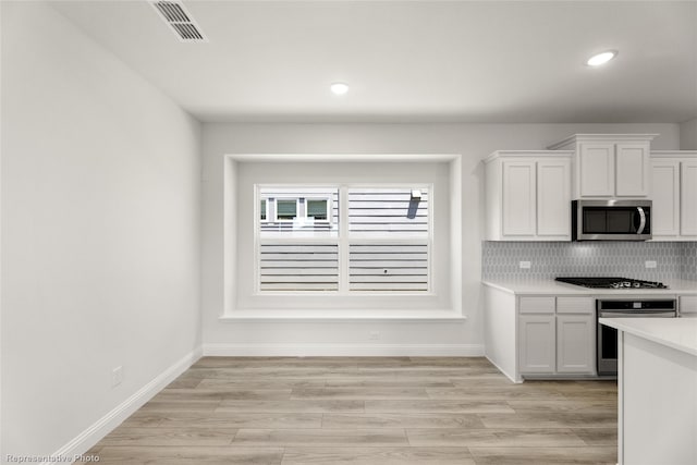 kitchen with white cabinets, light wood-type flooring, stainless steel appliances, and tasteful backsplash