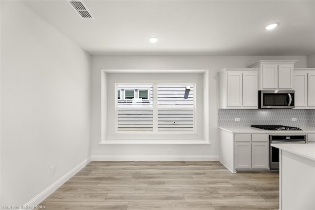 kitchen with stainless steel appliances, visible vents, white cabinetry, decorative backsplash, and light countertops