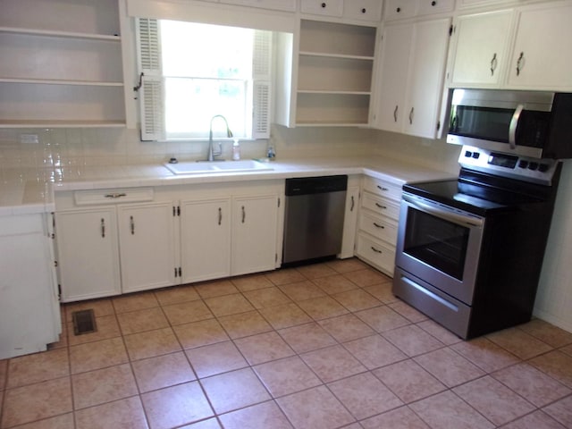 kitchen with sink, white cabinetry, light tile patterned floors, stainless steel appliances, and decorative backsplash