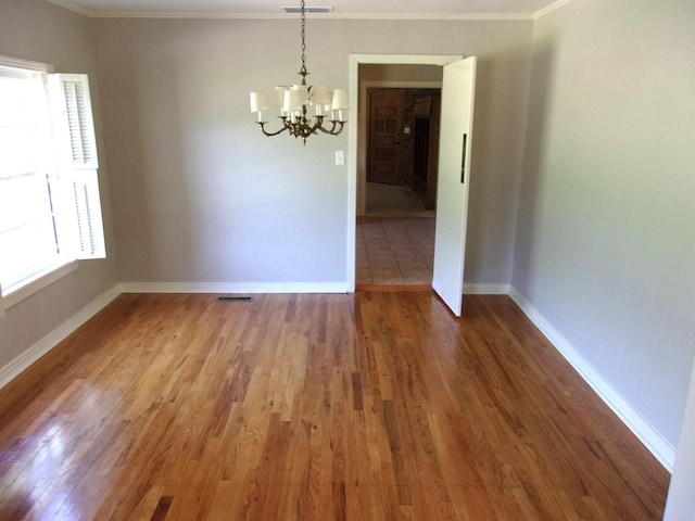 unfurnished room featuring a notable chandelier, hardwood / wood-style flooring, and ornamental molding