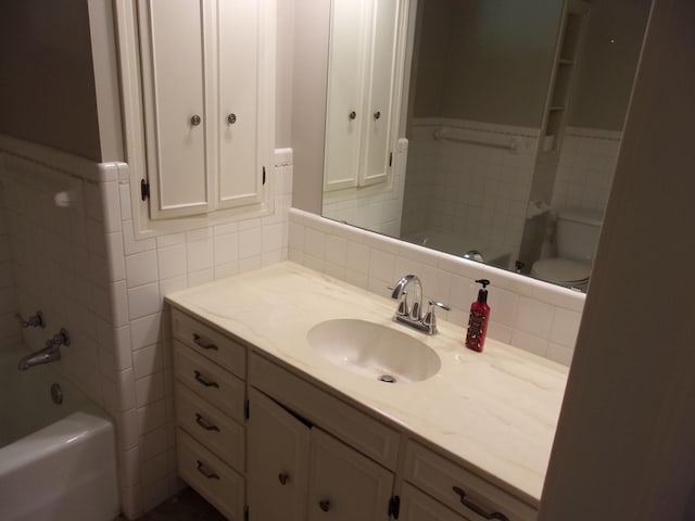 full bathroom featuring tile walls, vanity, toilet, and washtub / shower combination