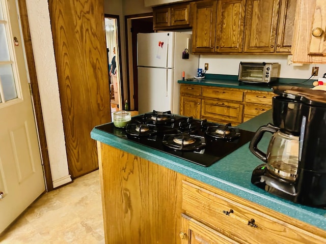 kitchen with a toaster, freestanding refrigerator, black gas cooktop, dark countertops, and brown cabinets